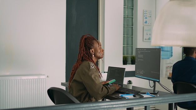 african american coder using computer to write code and develop algorithm program in software computer agency. web developer working on user interface with html script and terminal window.