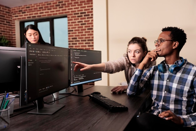 software developer asking coder for help with html code, pointing at database script on terminal window. team of programming engineers working on app developing program in data room.