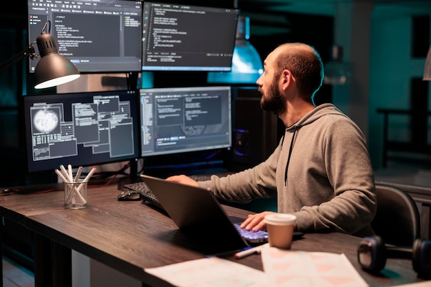 software developer coding database on multiple monitors to program new server interface at night. workign after hours to develop html source code on terminal window, artificial intelligence.