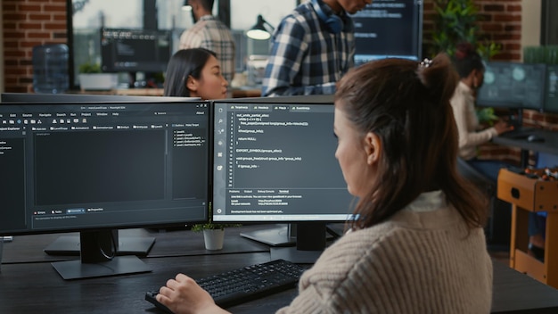 software programer writing code in front of multiple computer screens displaying artificial intelligence algorithm. developer coding database while colleagues doing online cloud computing.